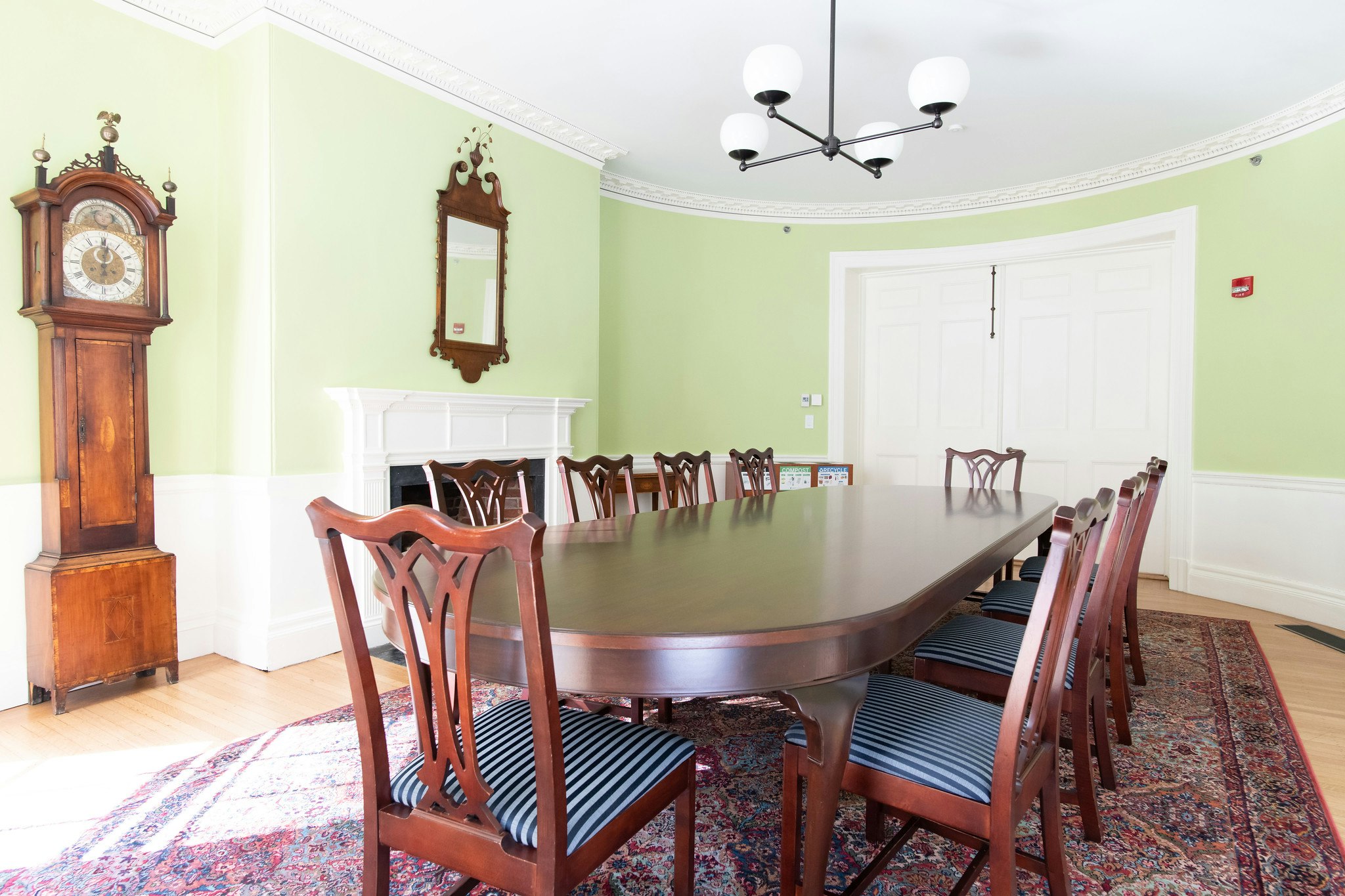 Another angle of the Gardiner Room, Conference table with 10 seats lined around table. Grandfather clock in the left corner of room. White, double door entrance on the other end of the conference table.