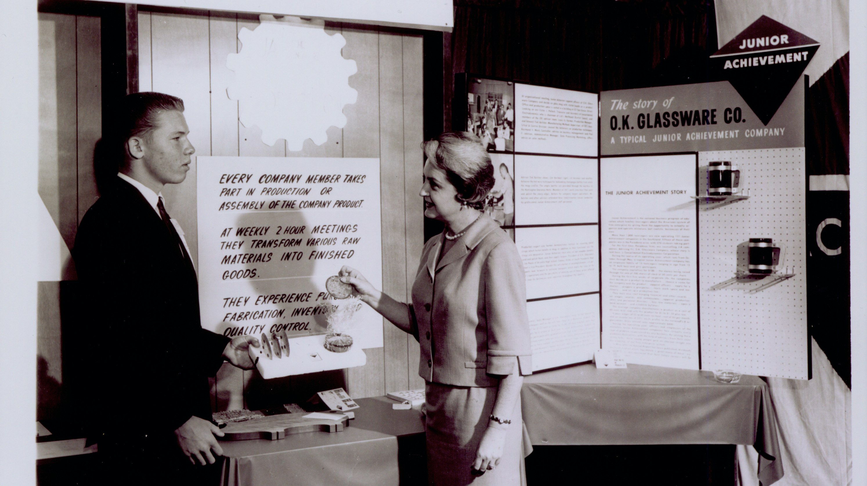 Ruth Handler at business convention standing with an unidentified man by a glassware display
