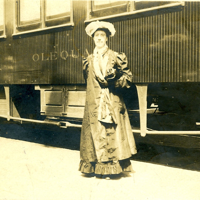 Portrait of Charlotte Perkins Gilman, standing outdoors in front of a train