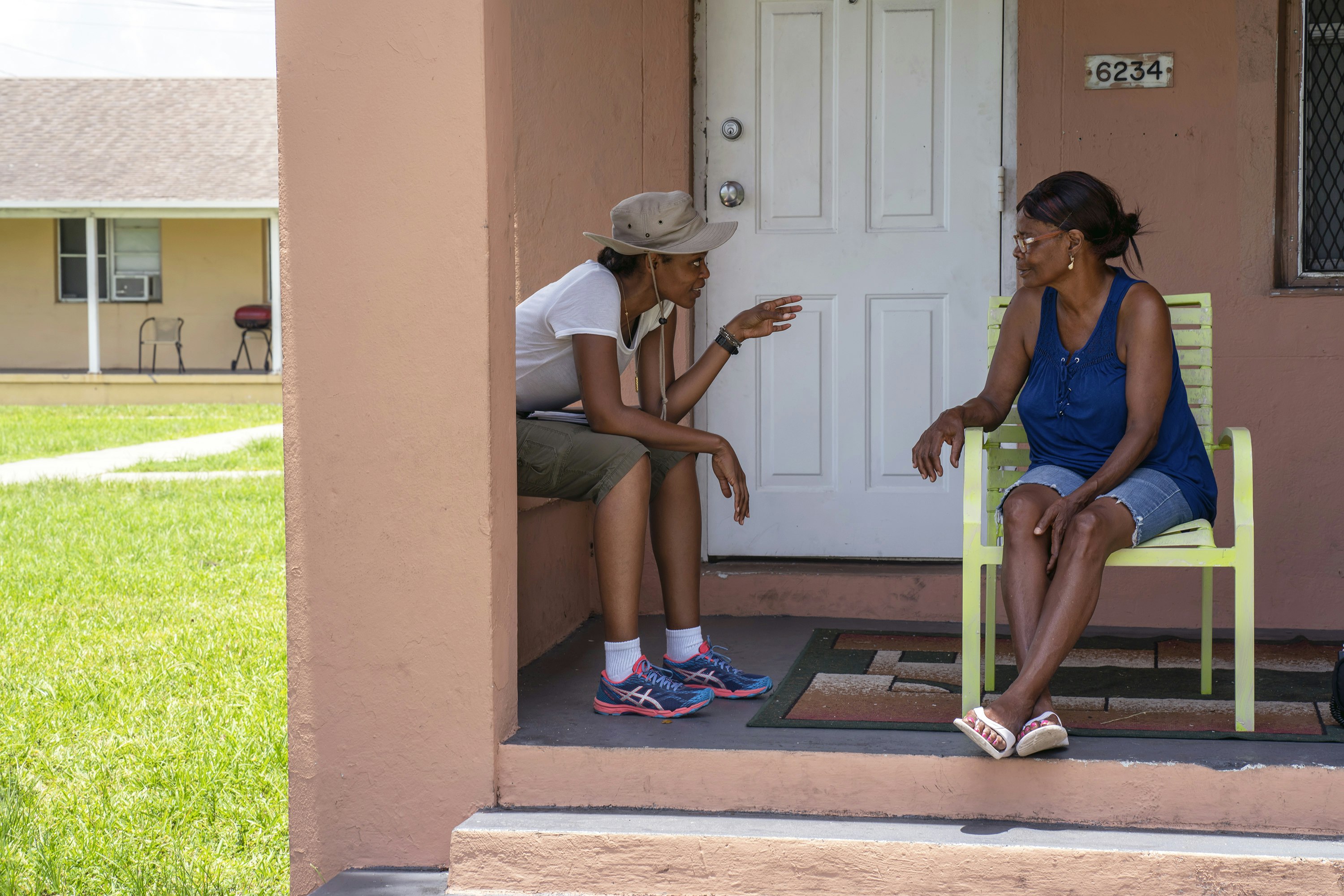 Faren Humes speaks to a woman sitting in a bright green chair on a Liberty Square porch