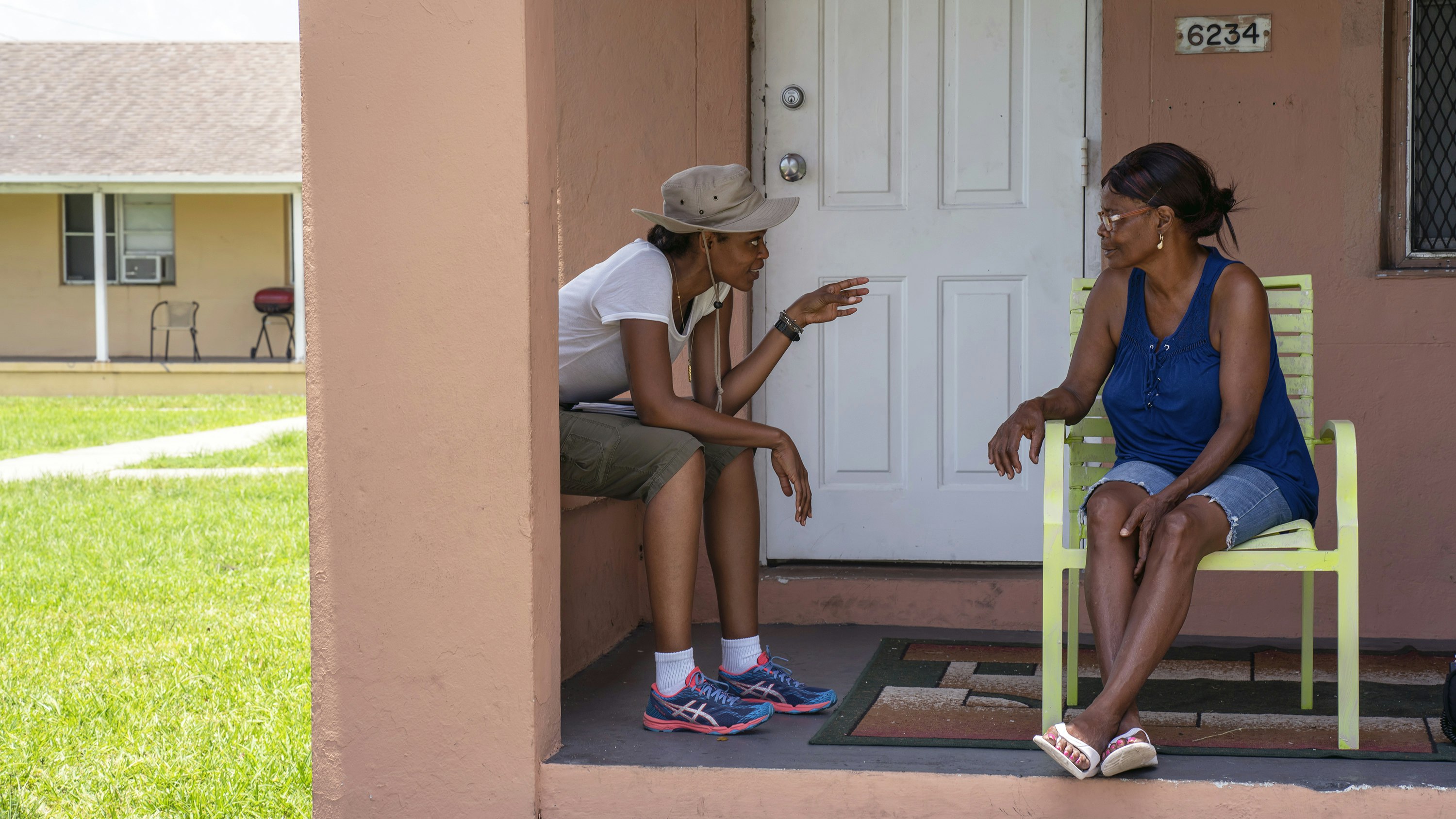 Faren Humes speaks to a woman sitting in a bright green chair on a Liberty Square porch