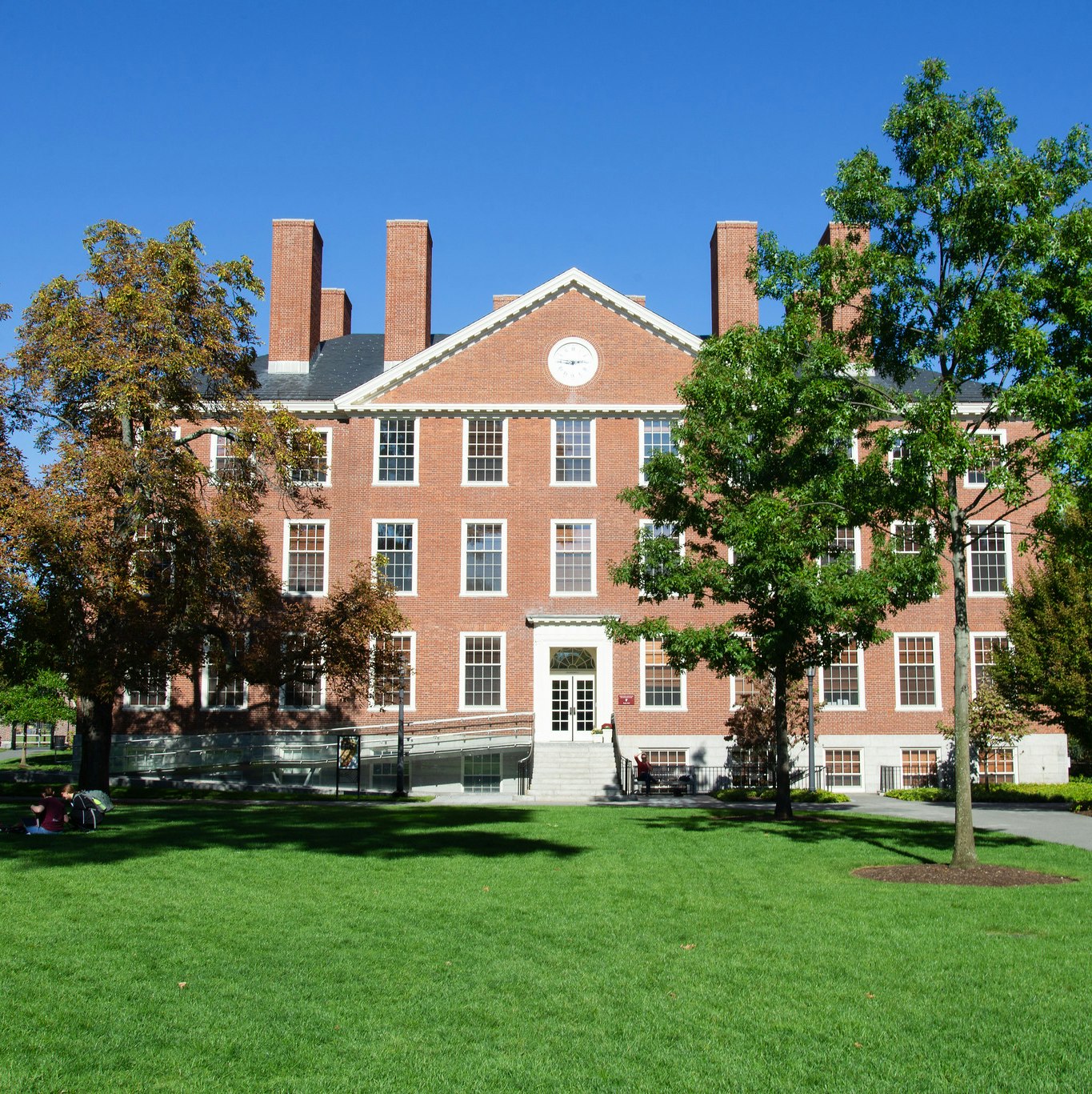 A brick office building with adjacent trees and green grass on a sunny day. The sky is blue.