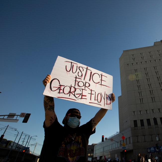 Man holding poster that reads "Justice for George Floyd." A building is in view