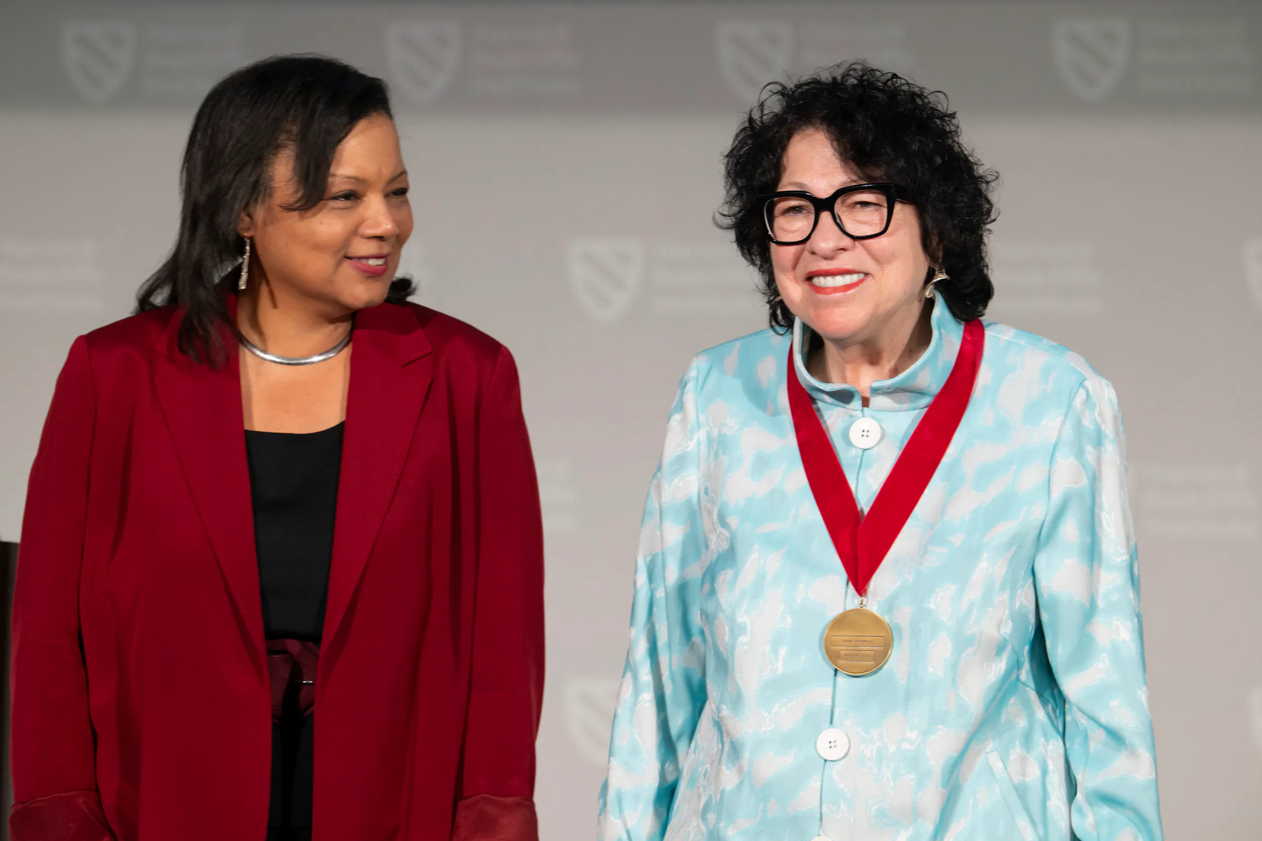 Sonia Sotomayor stands onstage, smiling, a medal on a red ribbon hanging from her neck.