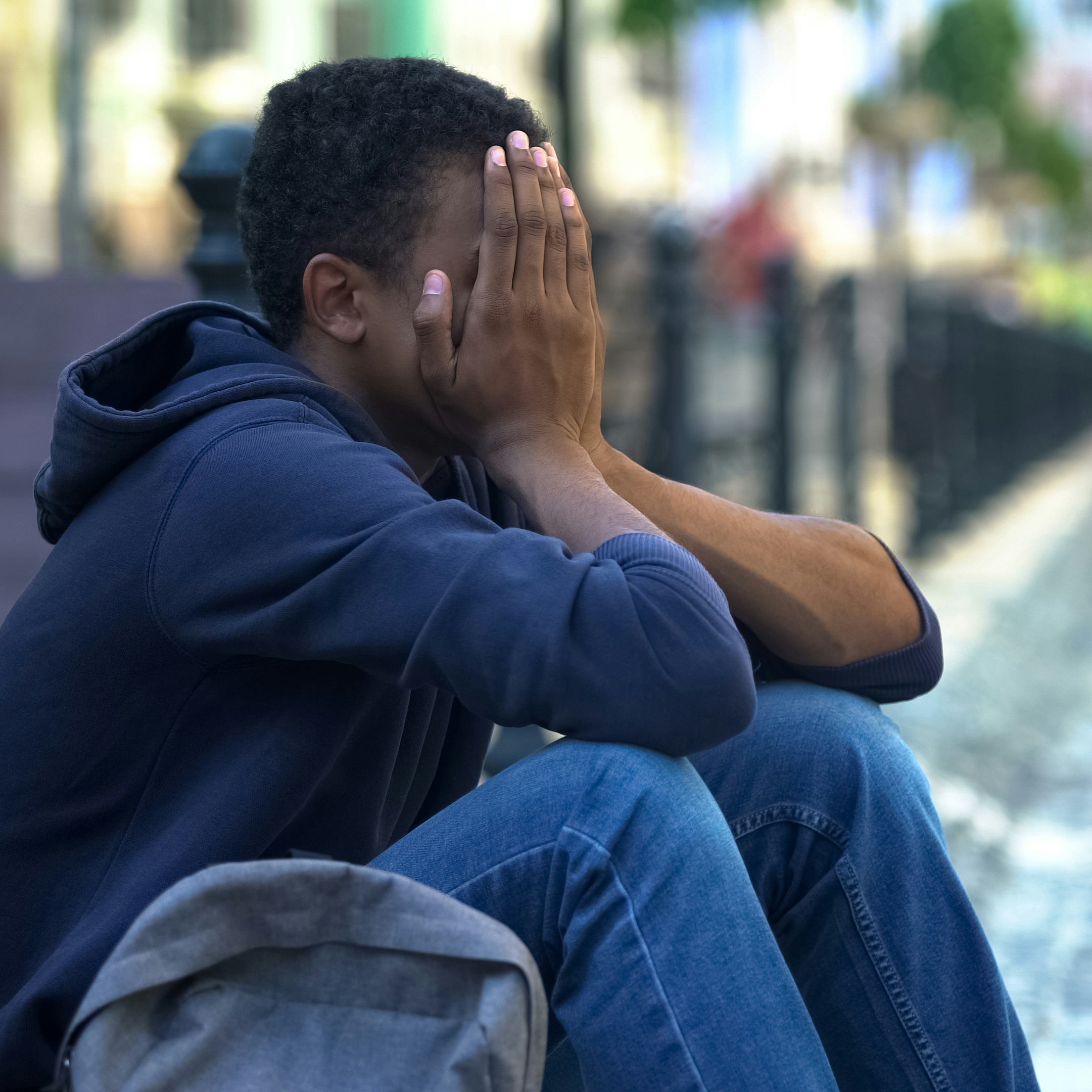 Depressed African-American male teenager sitting on city street, escape from home.