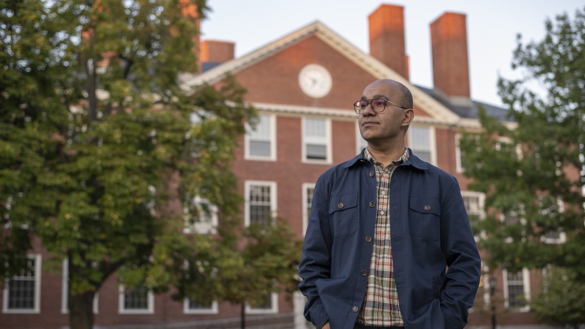 Rahul Bhatia stands Radcliffe Yard, Byerly Hall behind him, and looks to the upper left distance.
