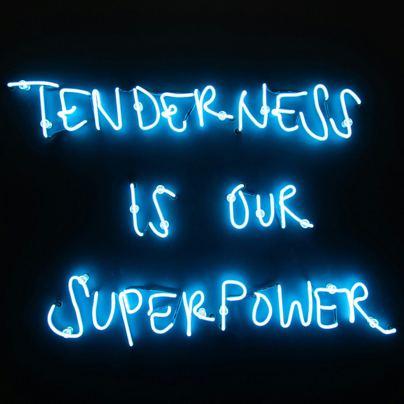 An image of a black chalkboard with white neon writing that says "Tenderness is our Superpower."