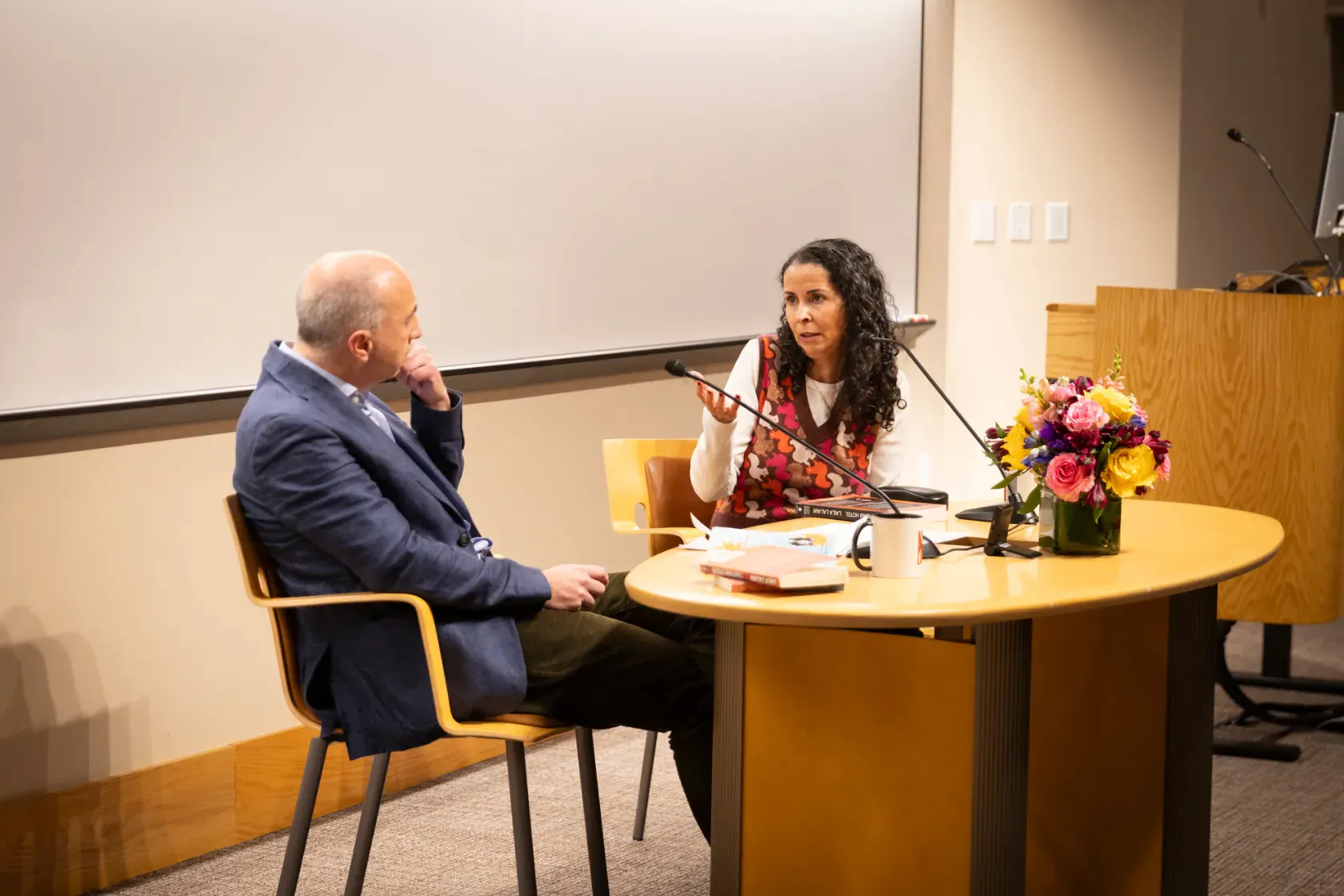 A woman sitting behind a desk talks as a man listens