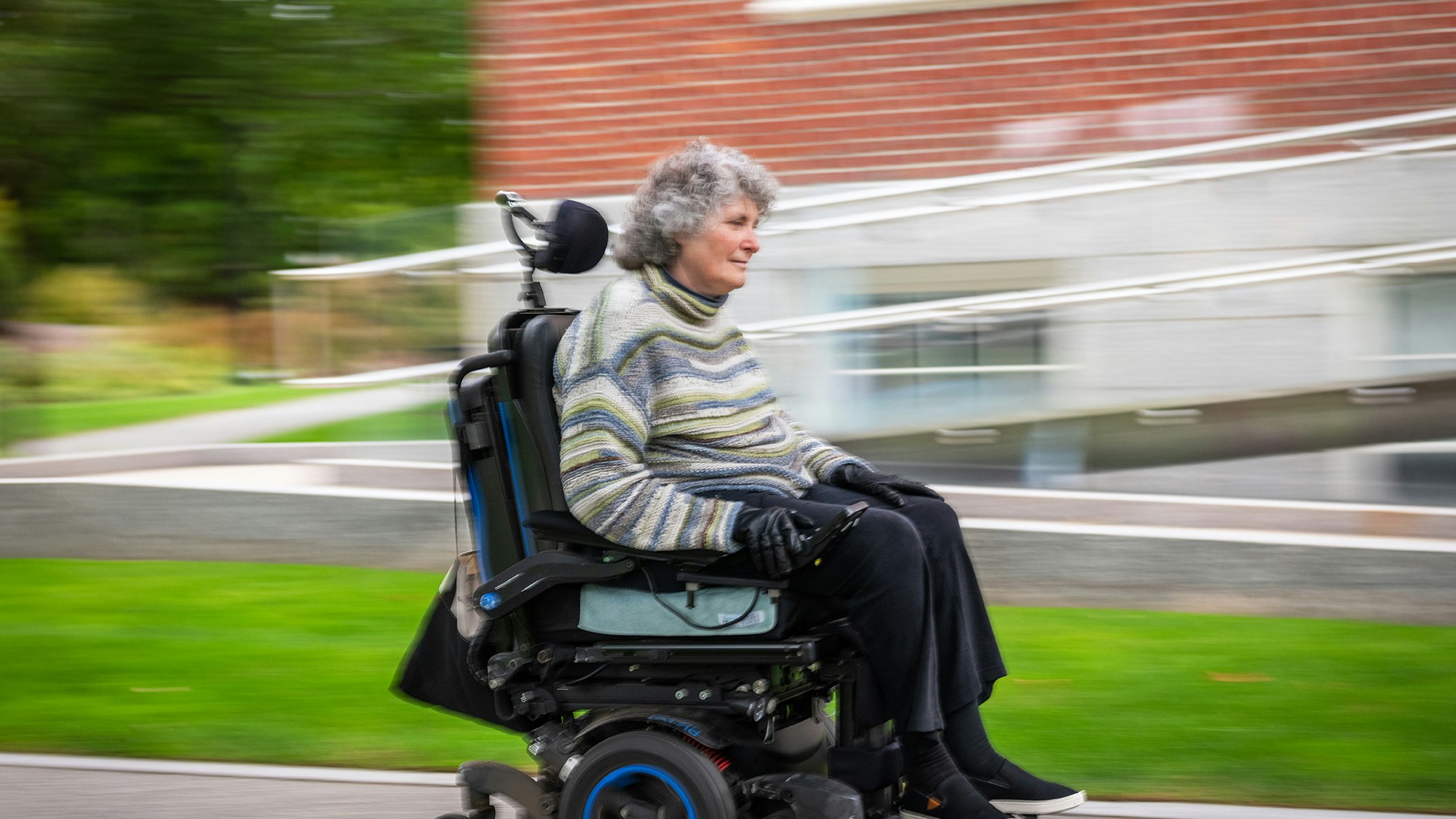Lisa Iezzoni in wheelchair riding past Byerly Hall in Radcliffe Yard.