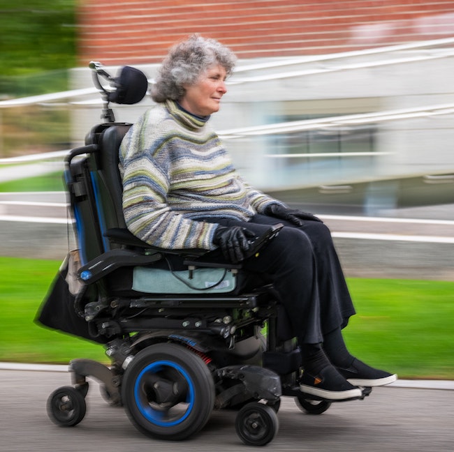 Lisa Iezzoni in wheelchair riding past Byerly Hall in Radcliffe Yard.
