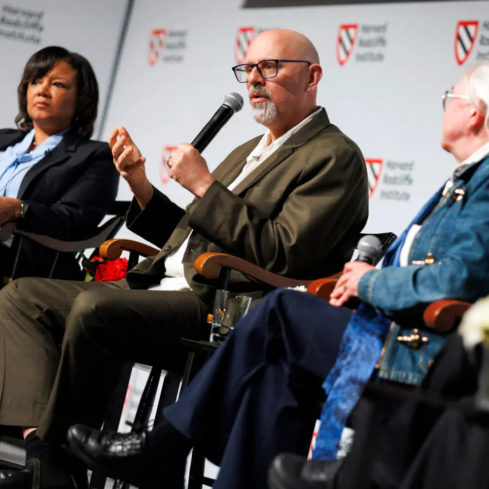 A man seated between two women speaks into a microphone.