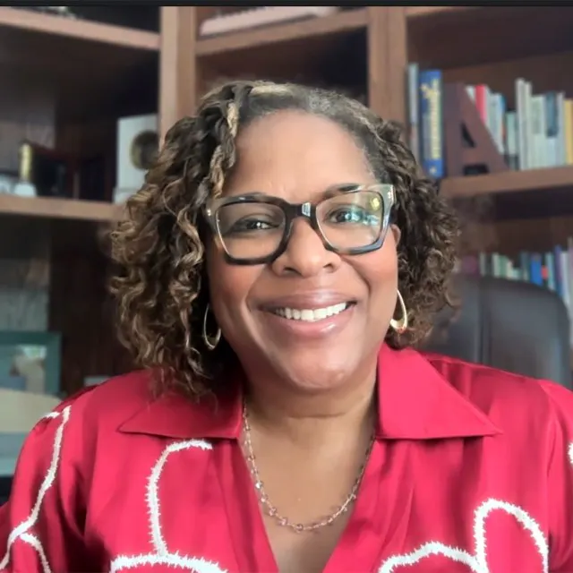 A bespectacled Black woman smiles in front of a bookcase.