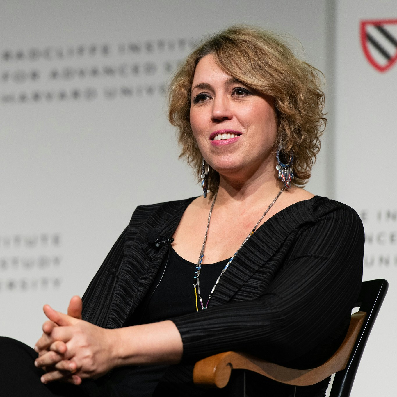 A woman sits in a chair on stage listening to an audience question.