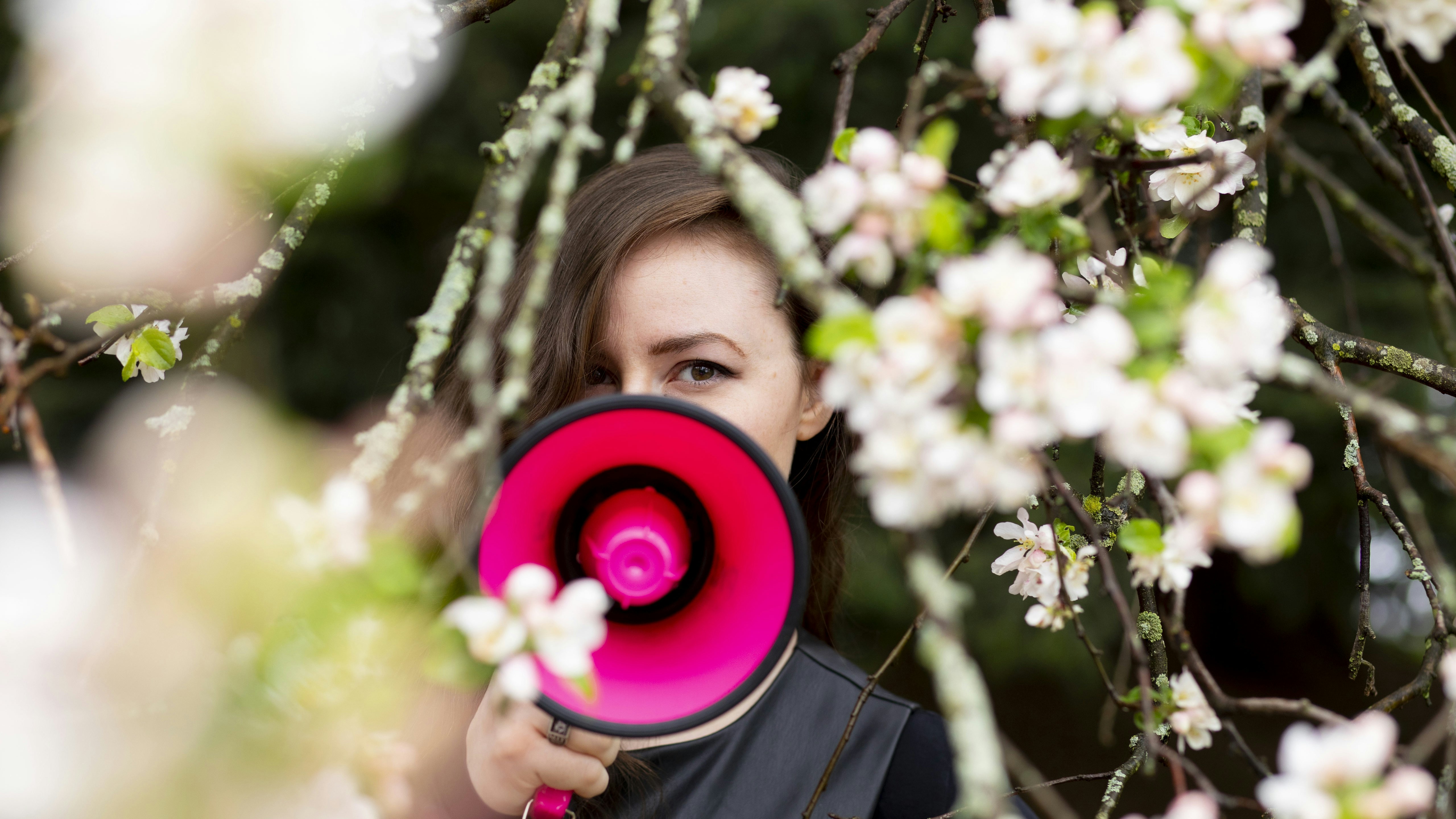 A woman stands among the lilacs, her face partially obscured by a fuchsia megaphone.