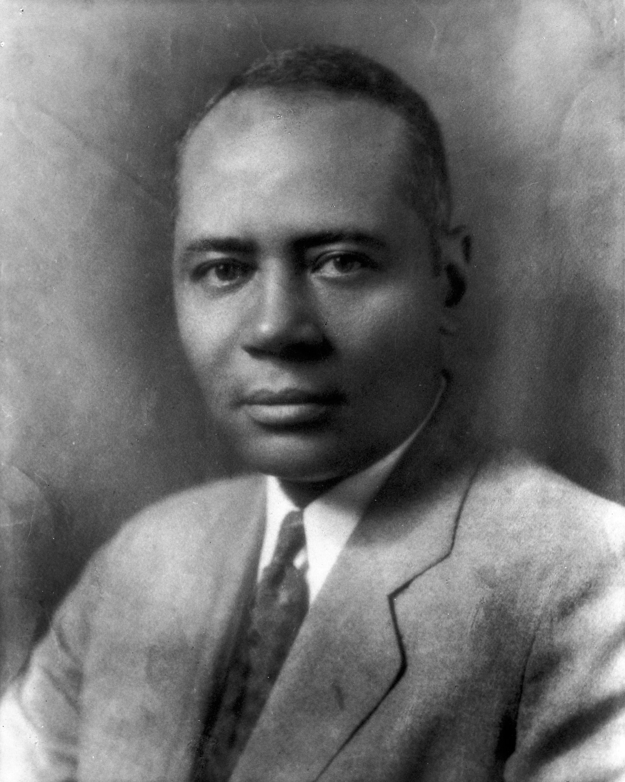 Dark black-and-white head shot of a young Charles Hamilton Houston. He wears a suit and tie and stares directly at the camera.
