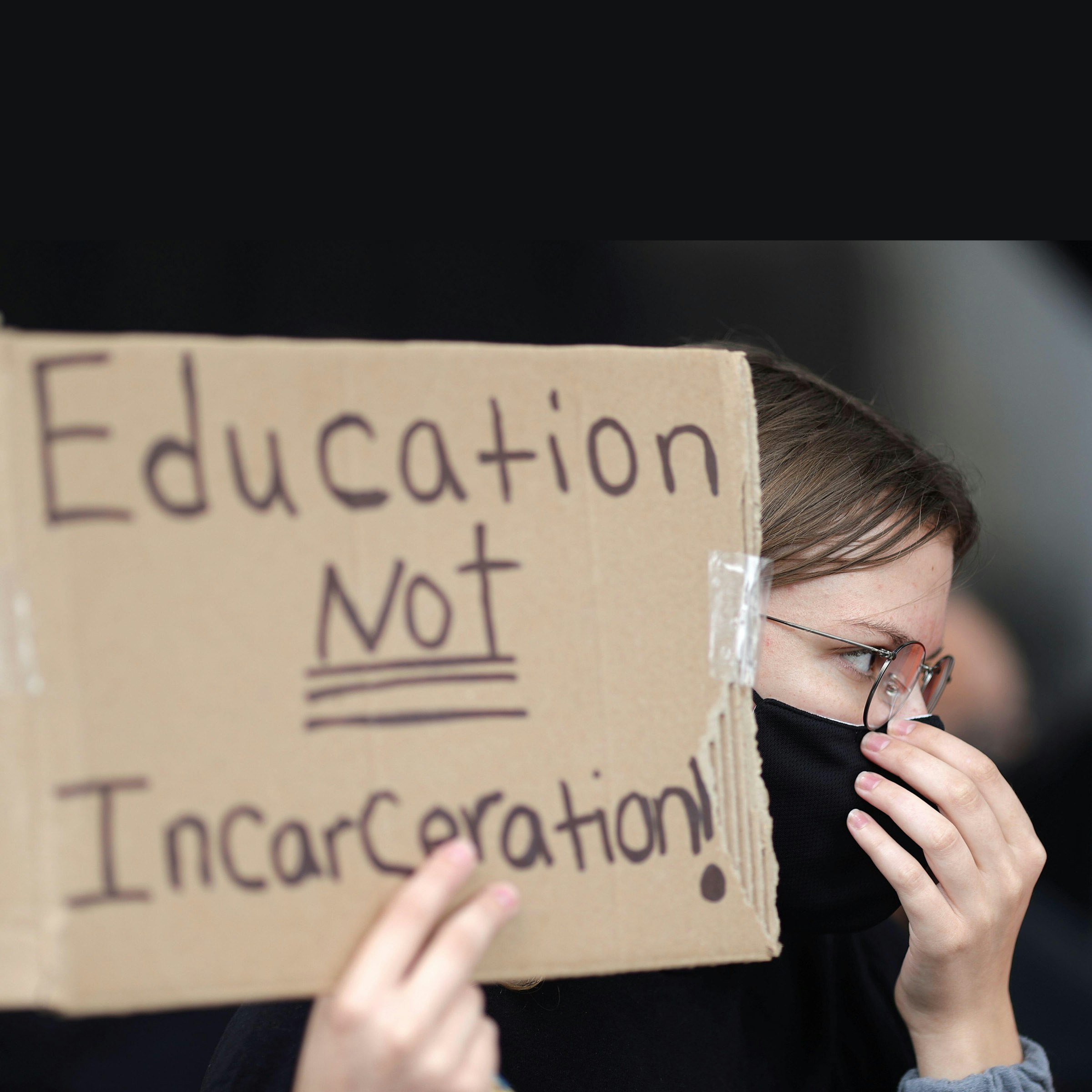 A person holds a placard that reads "Education NOT Incarceration"