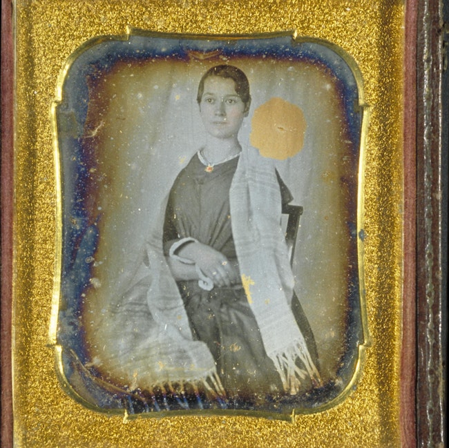 A discolored daguerreotype portrait of Elizabeth Blackwell, wearing a white shawl, set in a an elaborate gold frame.