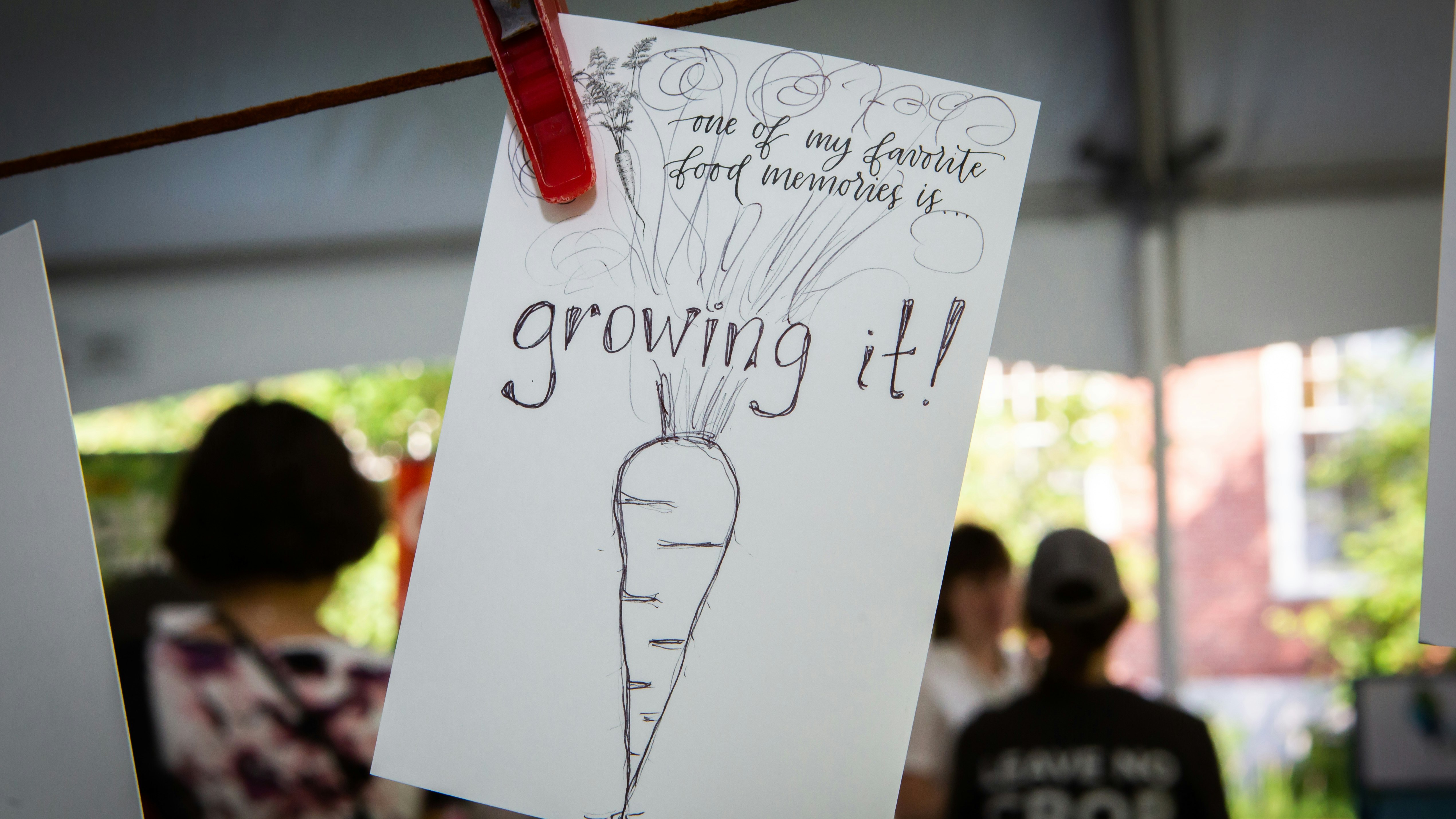 Piece of paper hanging by clotheline pin, with an illustration of a carrot and reading "one of my favorite food memories is.. growing it."