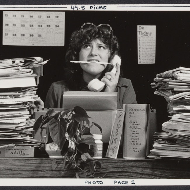 Woman posing at a desk with piles of paper stacked around her