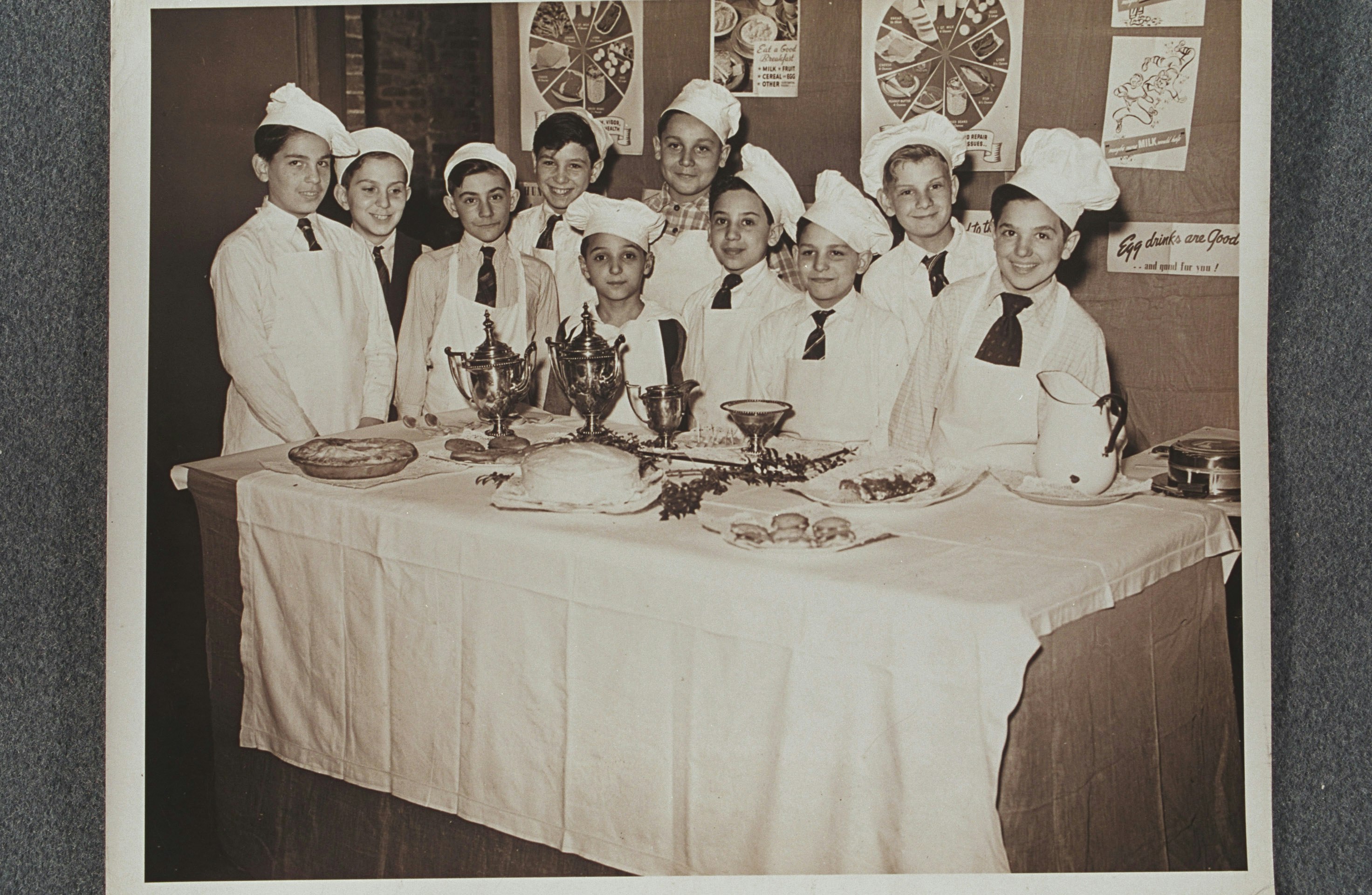 Portrait of ten boys in cooking class, standing in front of nutrition poster display and behind table of food