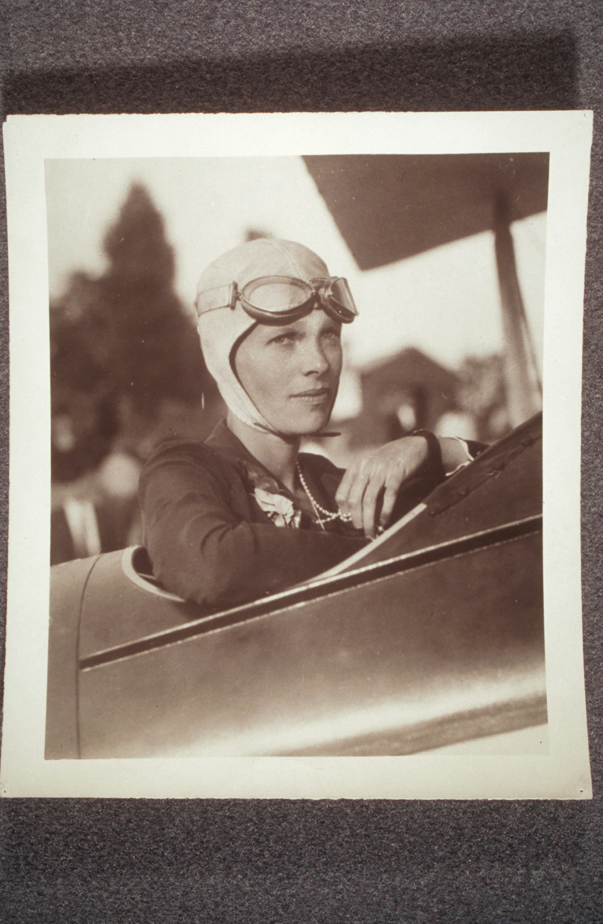 Amelia Earhart, in plane, wearing flight helmet and pearls
