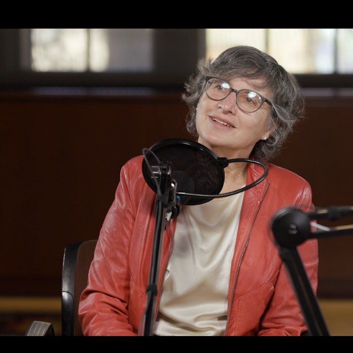A woman wearing glasses speaks into a microphone during a podcast recording.