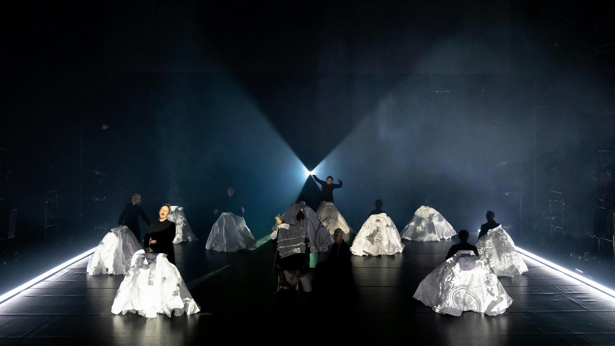 Several women wearing black perform behind giant paper ball skirts on a dramatically lit stage.