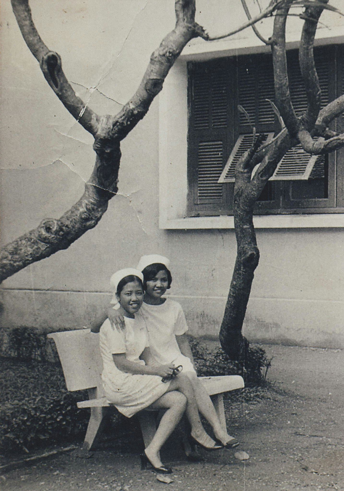 Sepia toned image of Hồng-Ân Trương's mother and her classmate sitting on a bench at 17 years old.