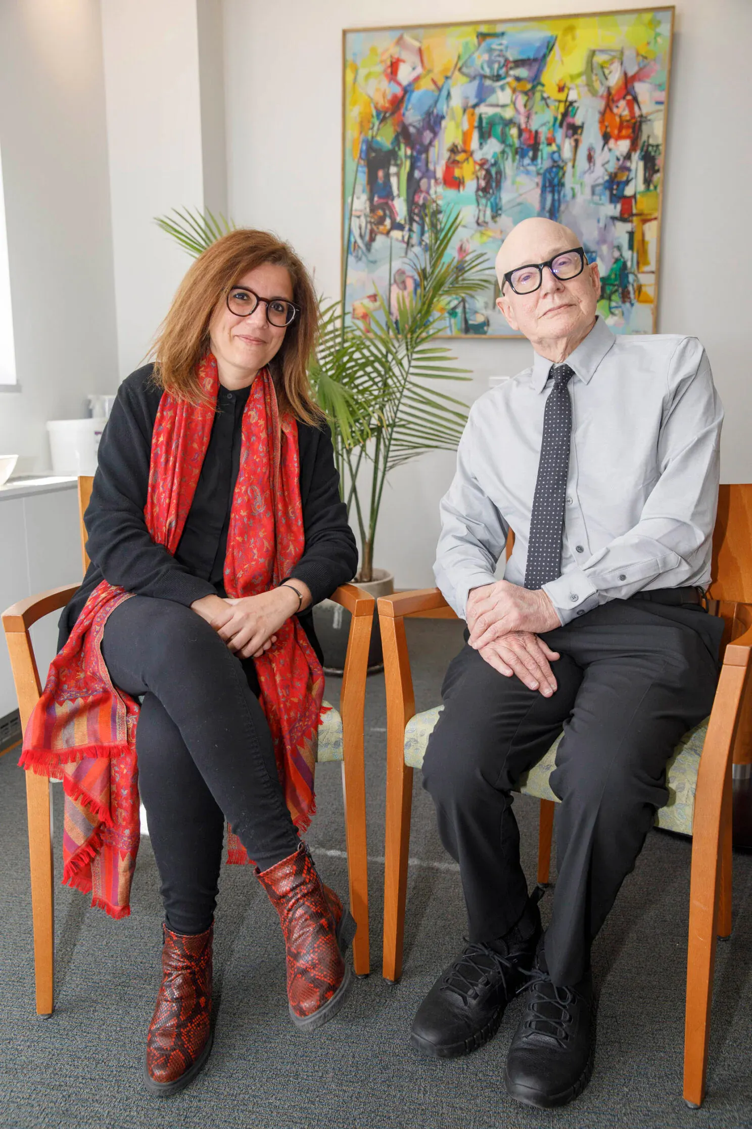 Joelle Abi-Rached and Allan Brandt sit next to each other, smiling, in front of a colorful painting.