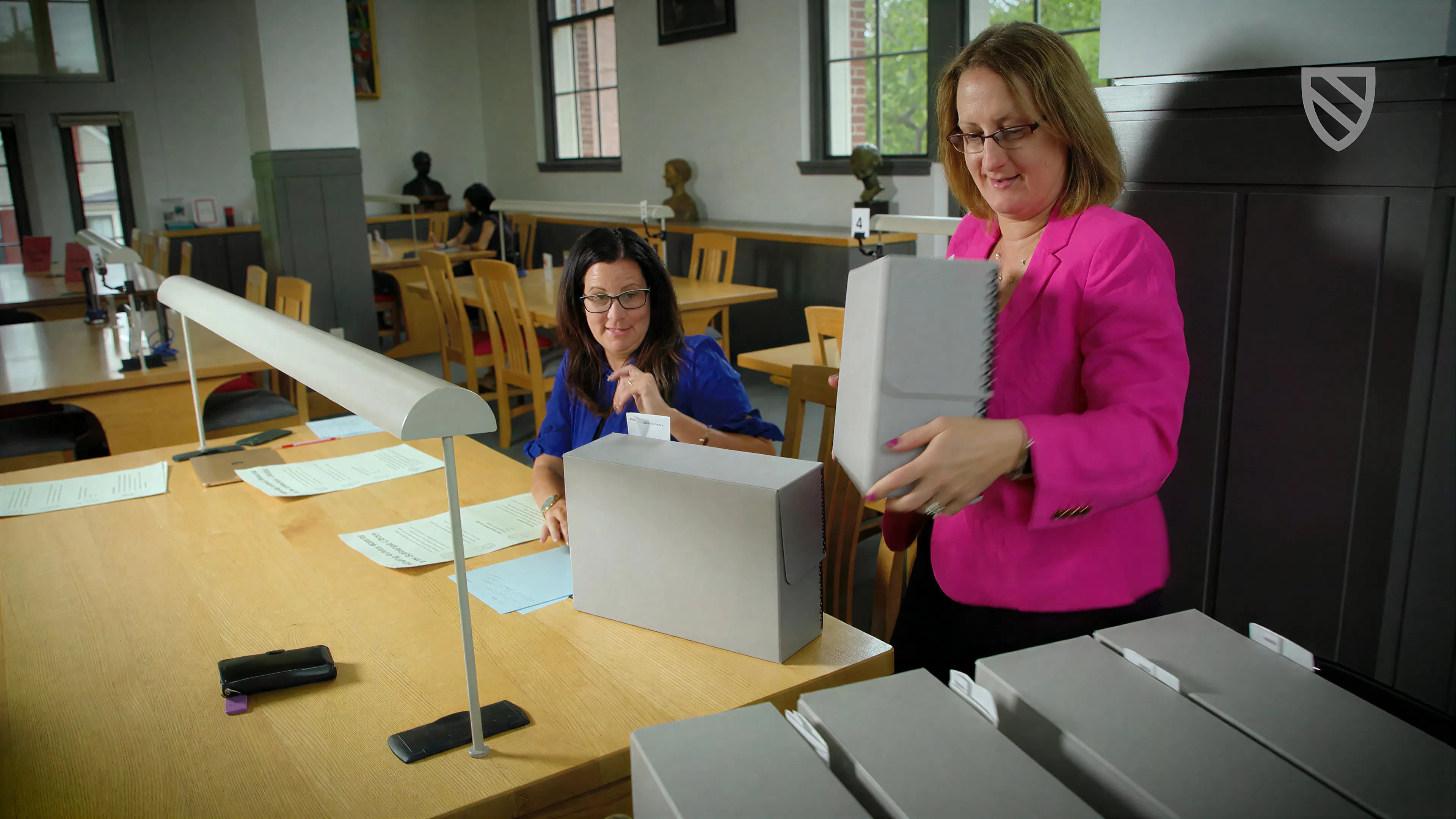 Two women examine archival materials at library reading room