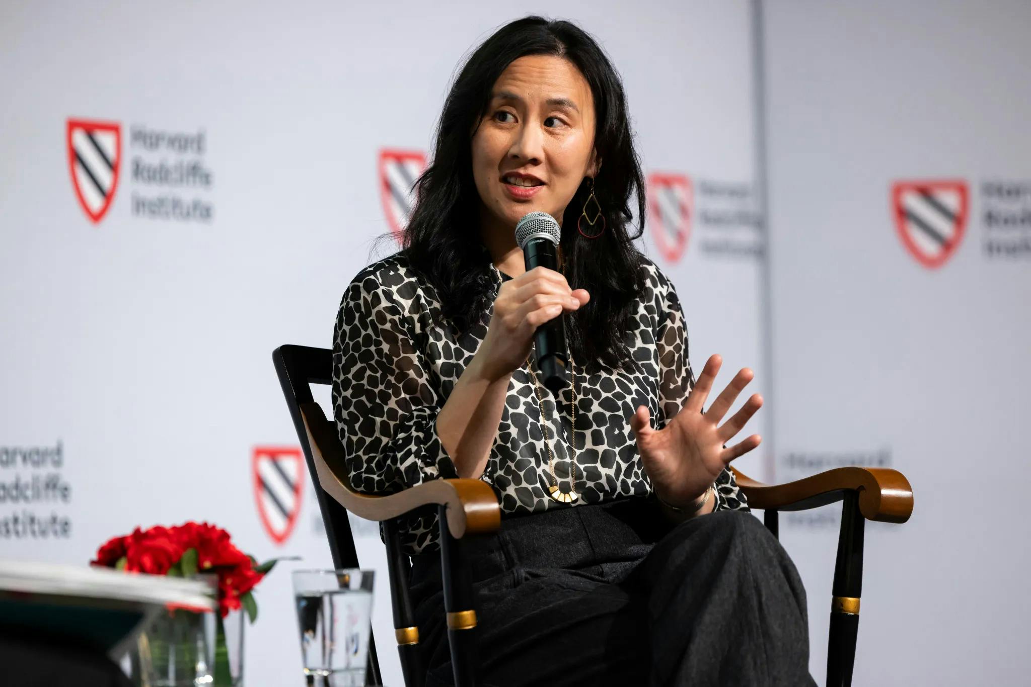 An Asian woman speaks into a microphone in front of a Harvard Radcliffe Institute–branded backdrop