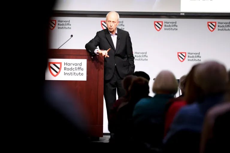 Sandel onstage in a suit, speaking while leaning against the lectern.