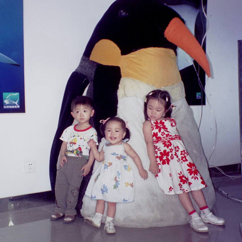 Childhood Vanessa Hu with two other family members leaning on large stuffed animal penguin