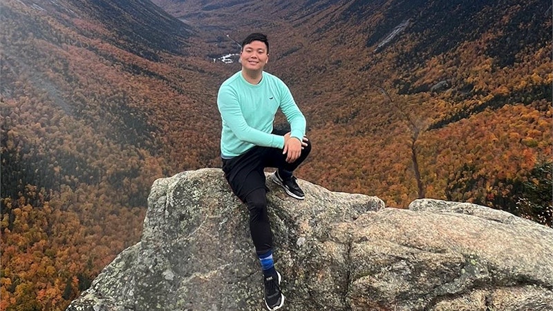 Jonathan Zhang sits on a rock overlooking a forested valley