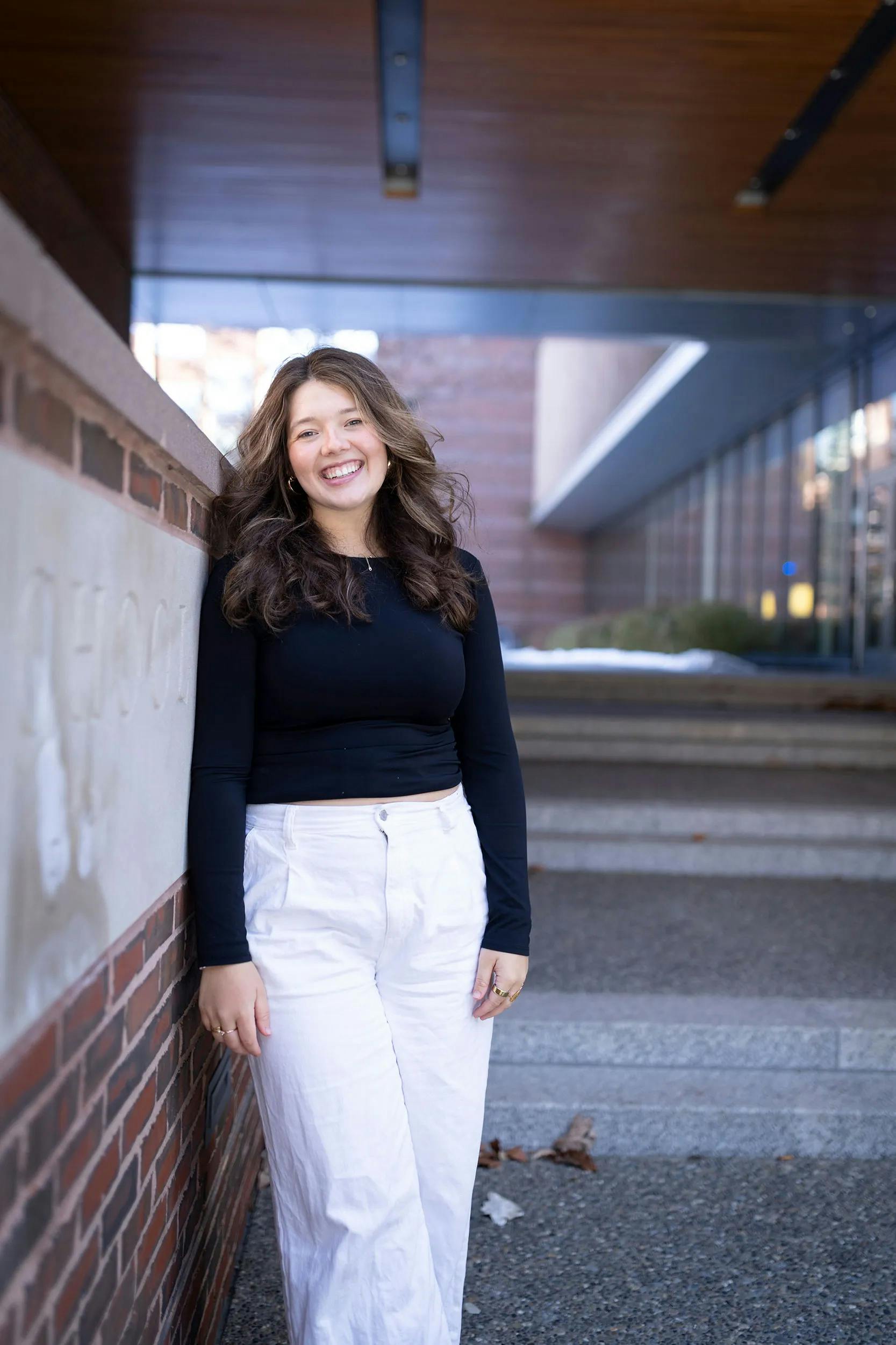 A smiling young woman leans against a brick wall.
