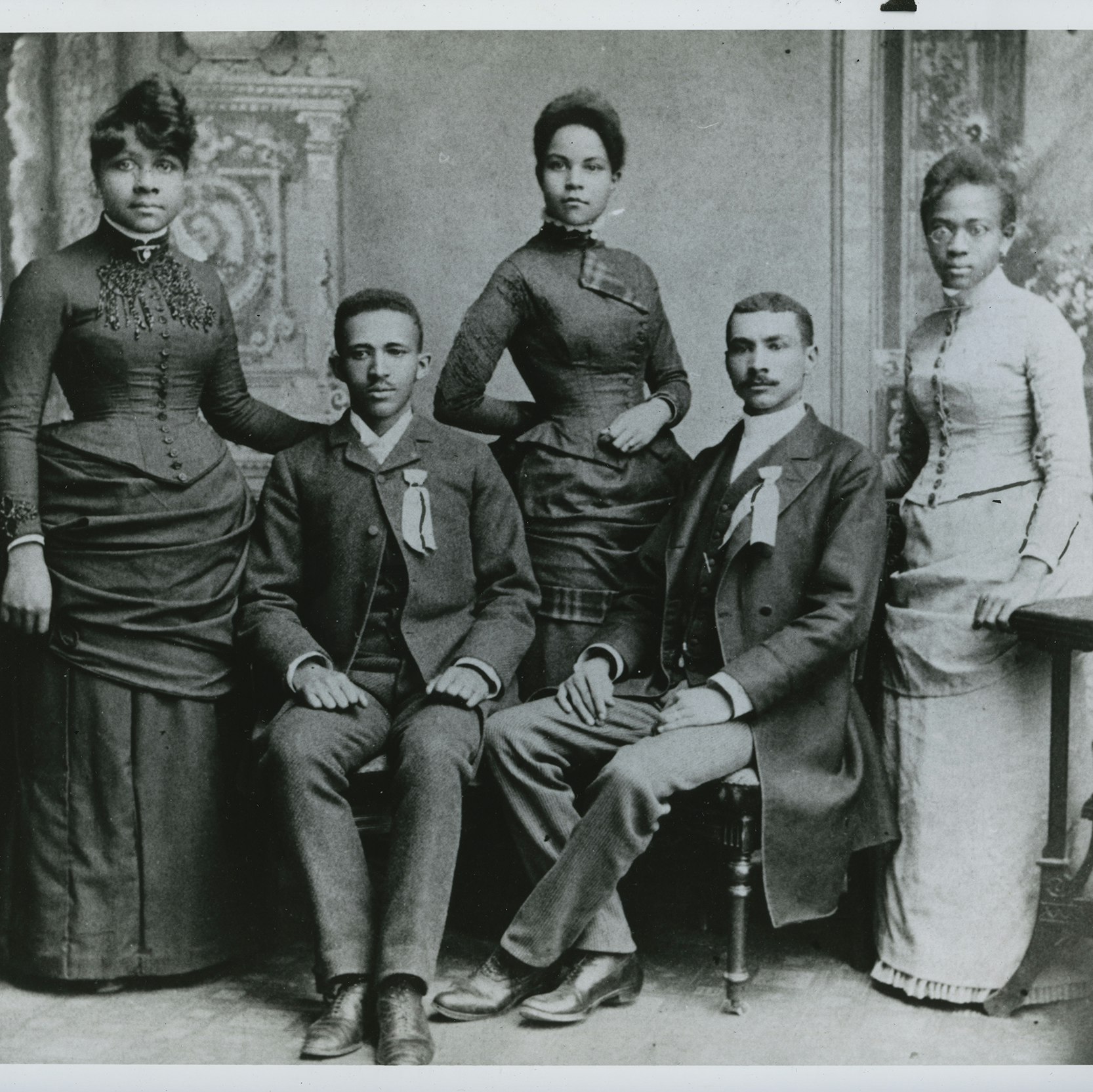 Black-and-white photo of Du Bois with Fisk classmates: three young women, standing, and two young men, seated, including Du Bois.
