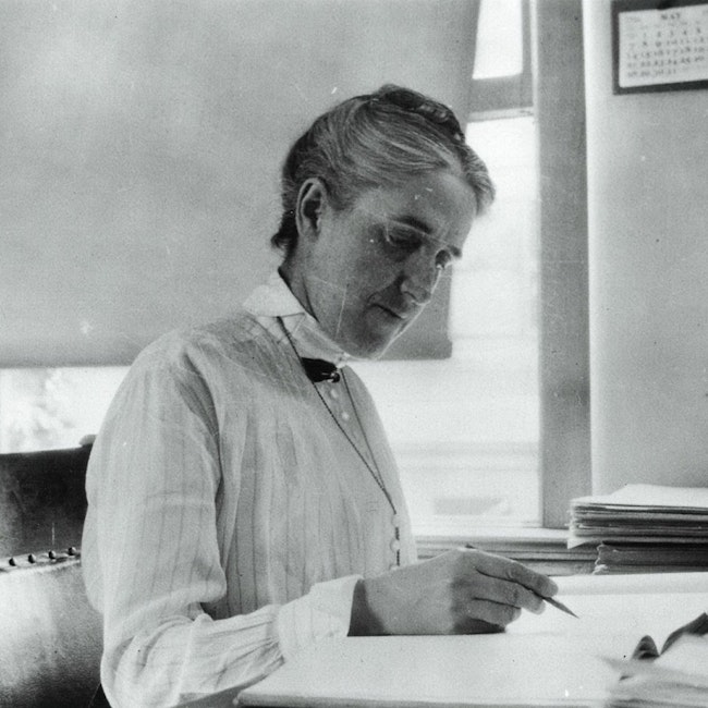 Woman sitting at a desk, pencil in hand with a book open faced.