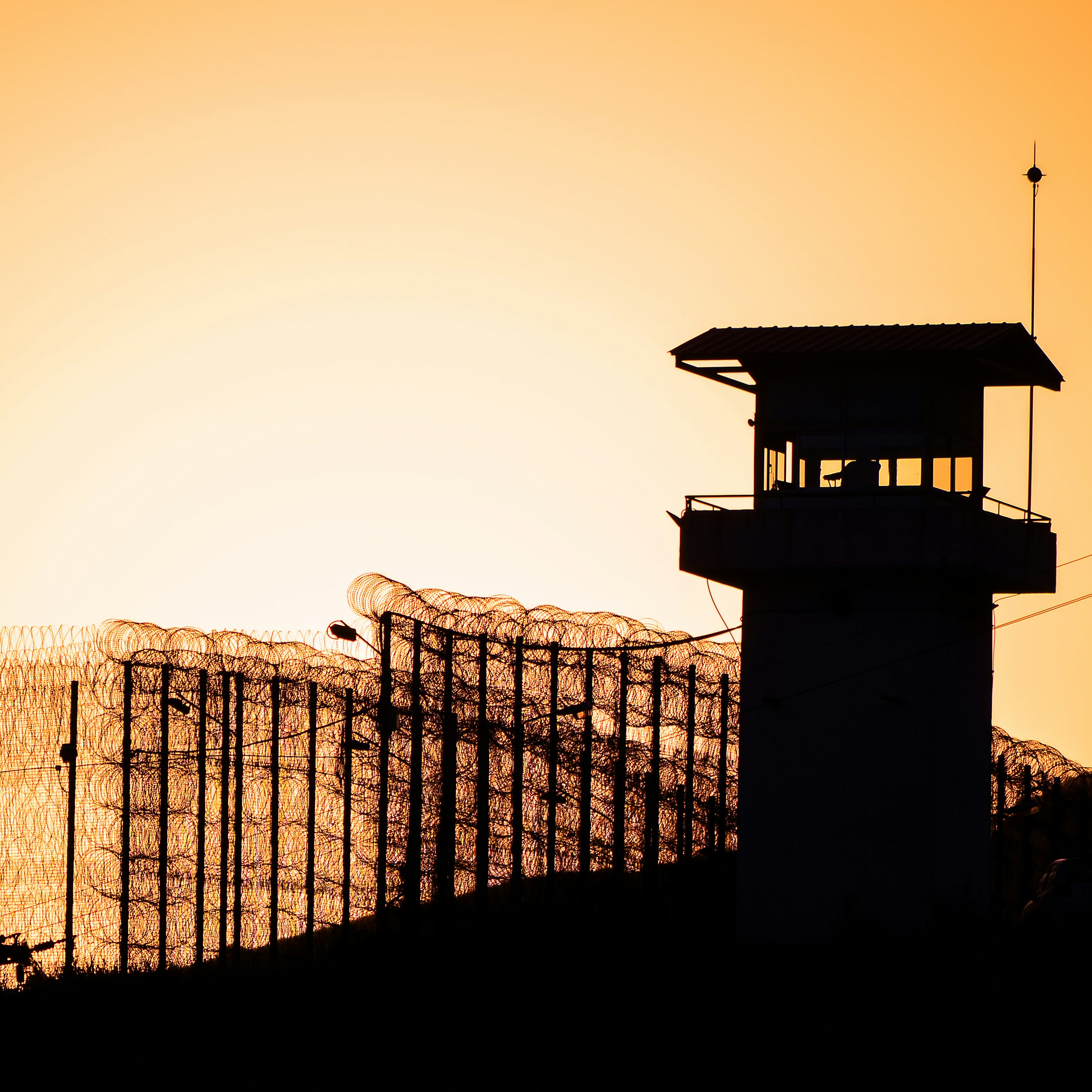 Silhouette of barbed wires and watchtower of prison.