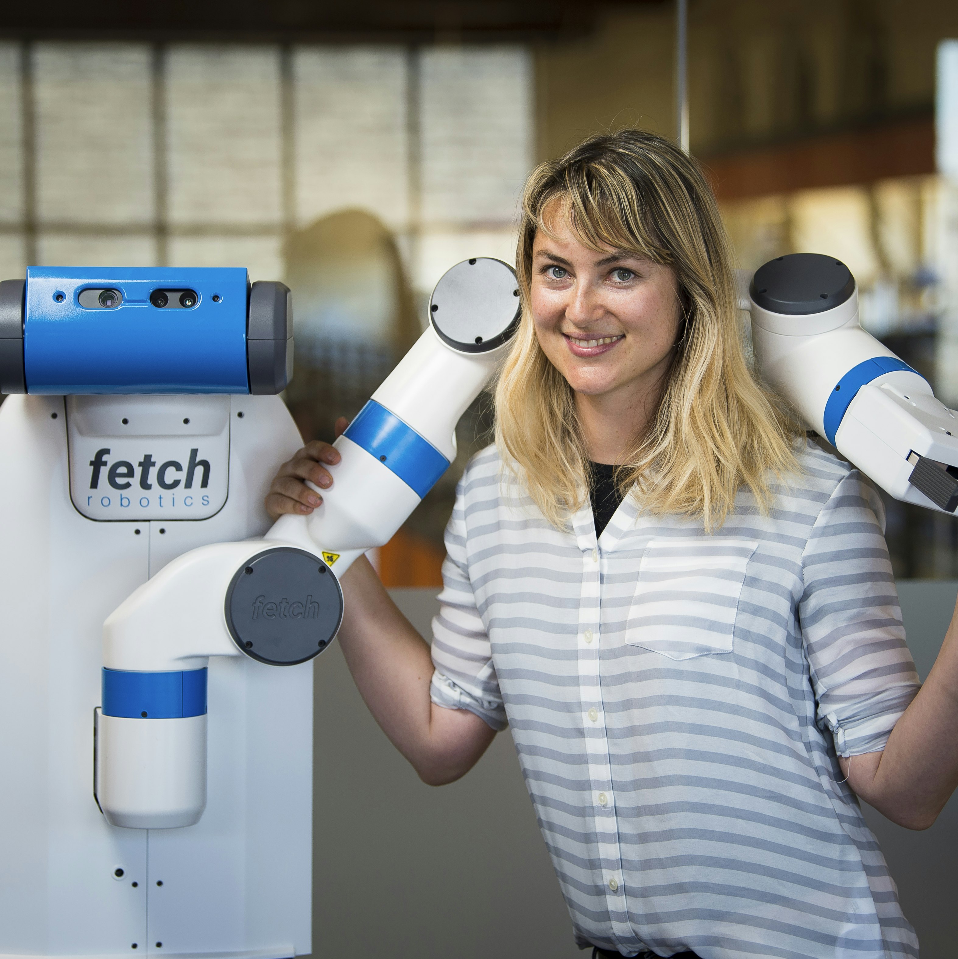 Heather Knight posing with robot's arm around her shoulders.