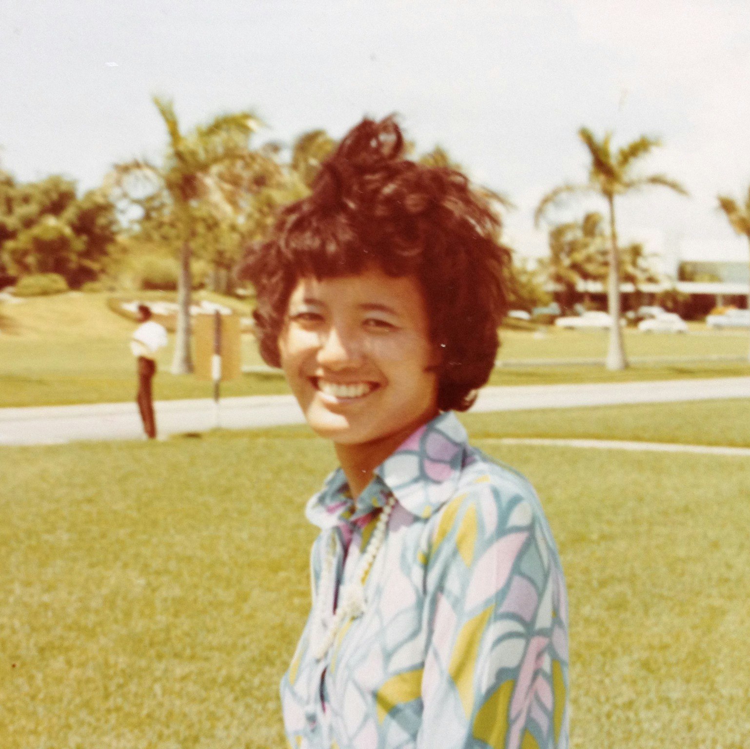 Headshot portrait of Denise Khor's mother outdoors in the Bahamas with palm trees in the background