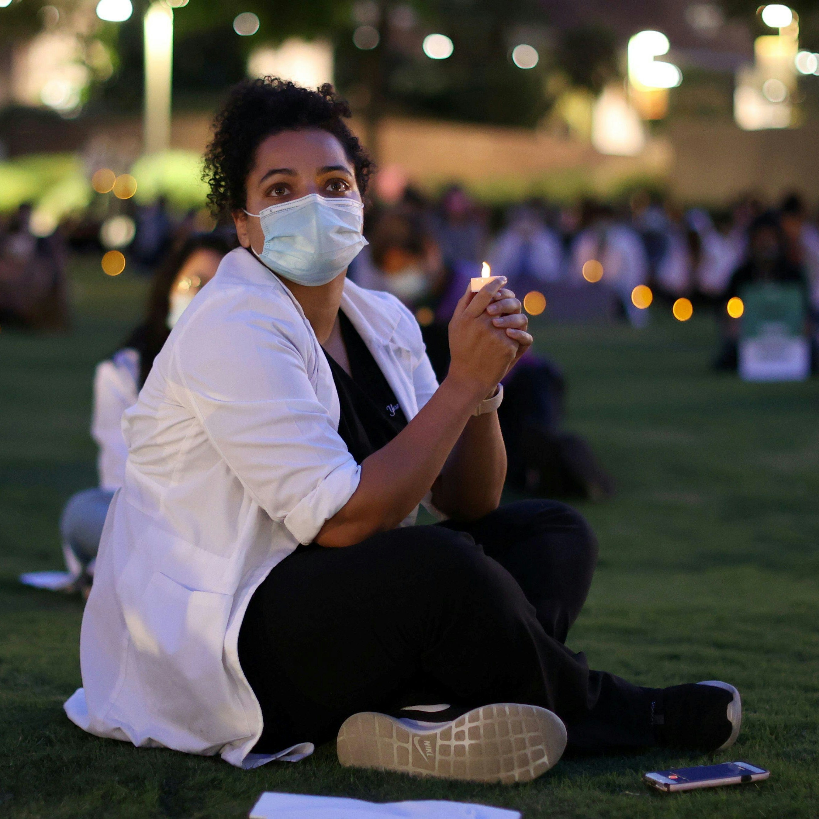 Student sitting on grass with candlelight, possibly at a vigil