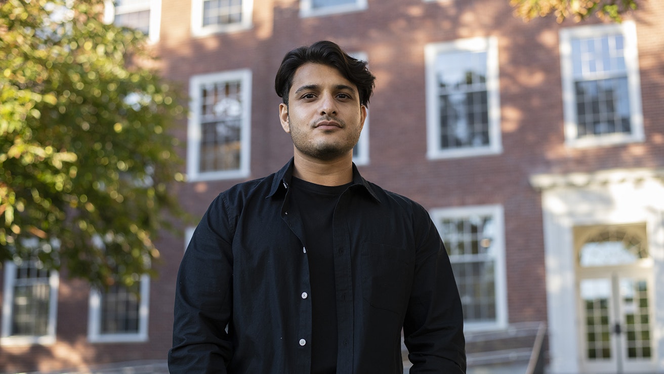 Omer Aziz looks seriously at the camera, hands in pockets; he stands outdoors in front of Byerly Hall.
