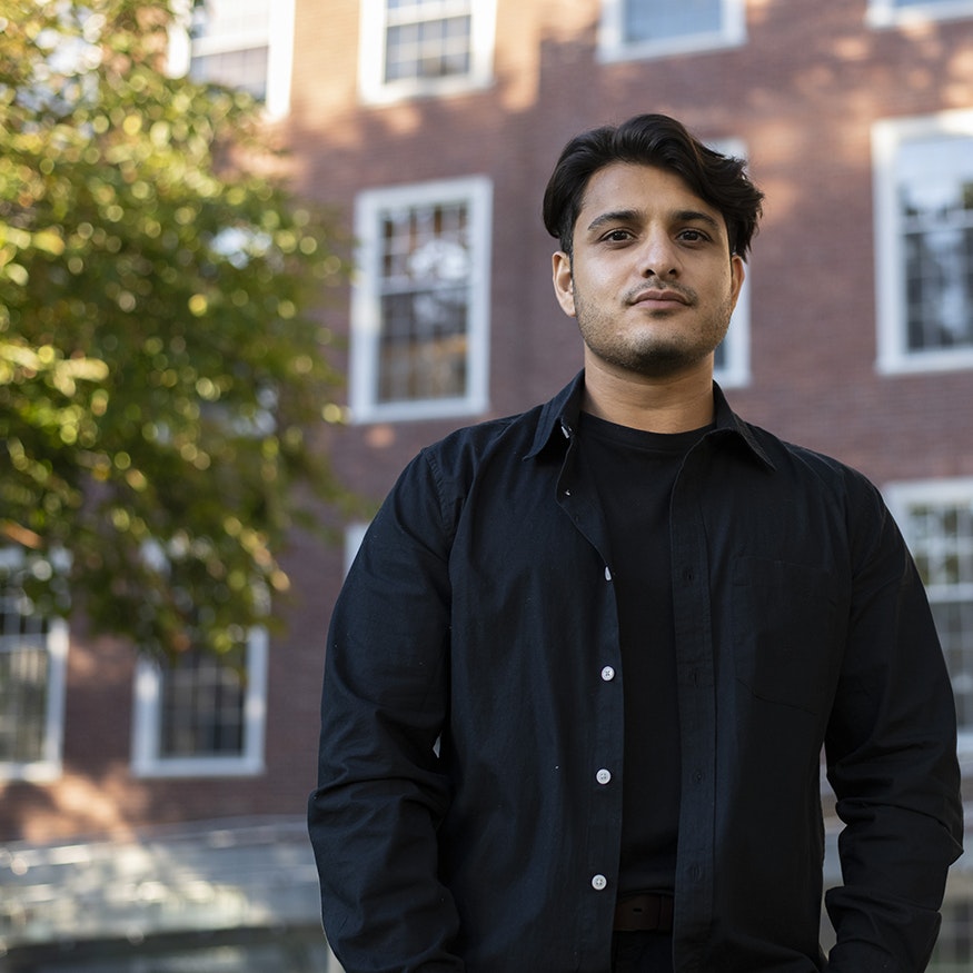 Omer Aziz looks seriously at the camera, hands in pockets; he stands outdoors in front of Byerly Hall.