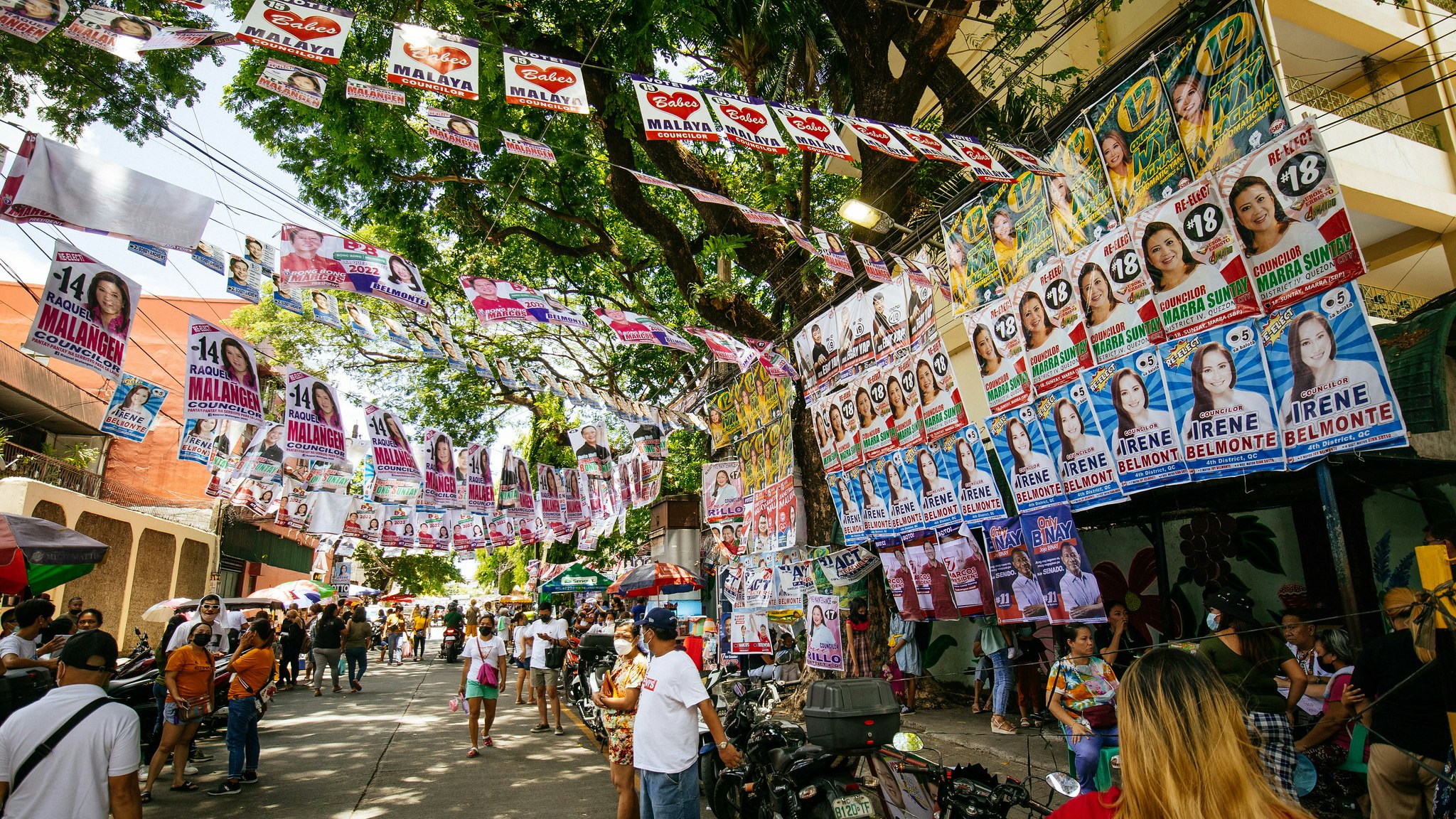 A crowded street scene; colorful flyers for political candidates hang over and across the street.