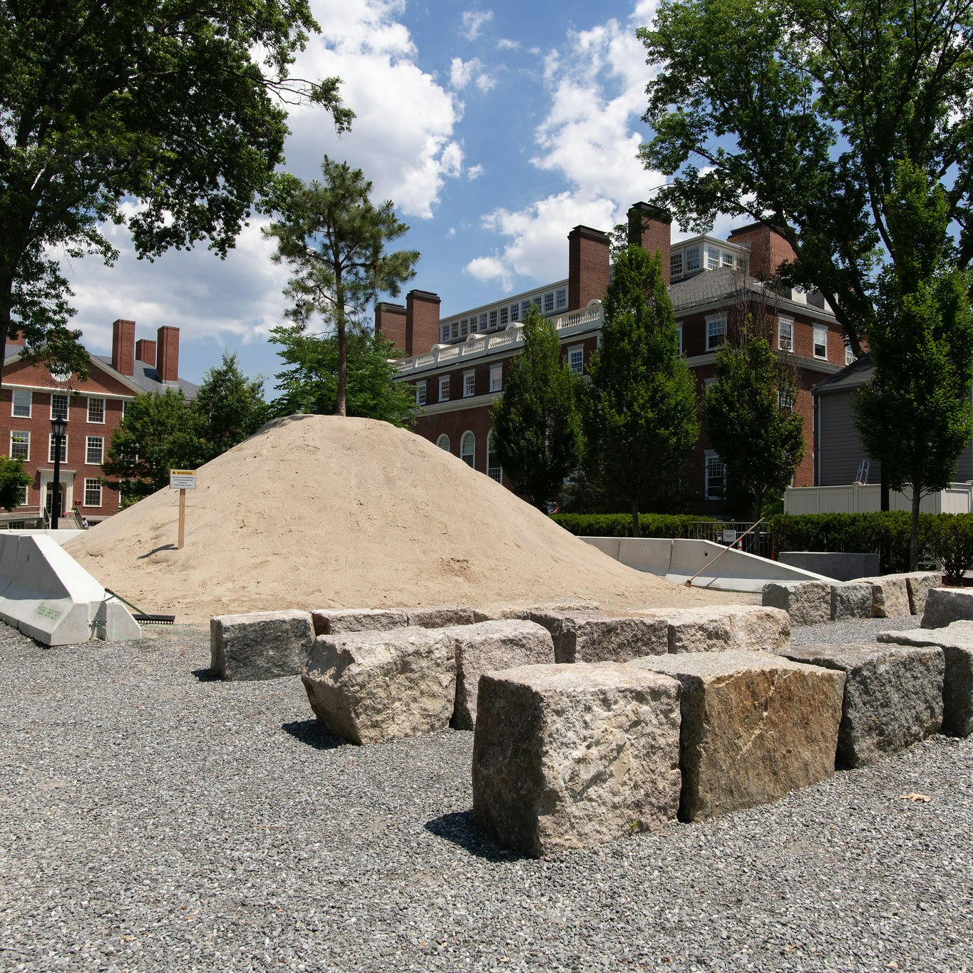 A mound of sand is planted with a pitch pine and partially contained by a ring of concrete barriers opposite rows of granite benches.